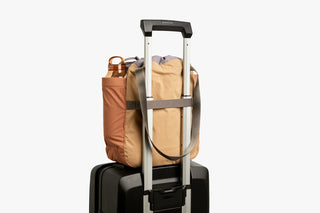 Tan cinch tote secured to a rolling suitcase handle for travel