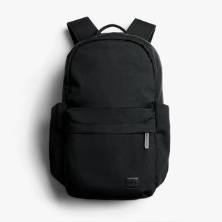 Black daypack with rounded top, front zip pocket, and small square logo patch
