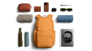 Orange daypack with front pocket and top zipper, accessories laid out beside it.