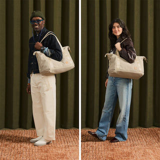 Beige canvas tote bag with handles, carried over the shoulder with front logo patch.