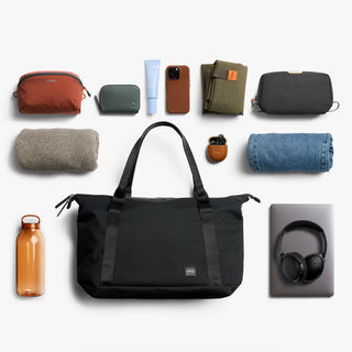 Black duffel tote bag centered in a flat lay, with dual handles and front zip pocket.