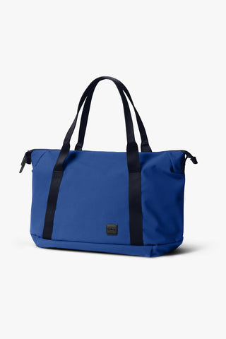 Indigo travel tote bag with black handles, front pocket, and zip top closure