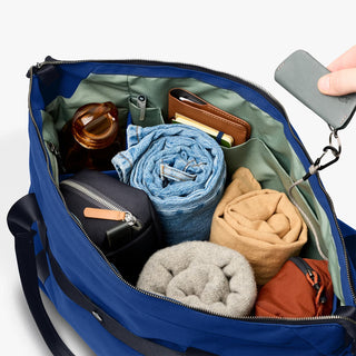 Indigo duffel bag open top with zipper, showing packed pockets and fabric rolls