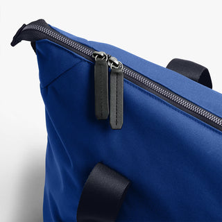 Indigo duffel bag close-up with metal zipper pull and side strap attachment