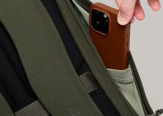 Olive green backpack with side pocket holding a brown smartphone, close-up