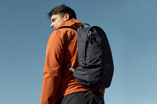 Black daypack backpack with padded shoulder straps, side view on a model