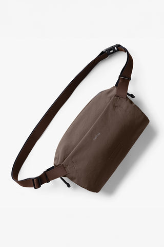 Brown fabric sling bag with adjustable crossbody strap and front zipper pocket.