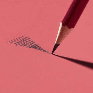 Matte red pencil tip drawing dark graphite lines on paper
