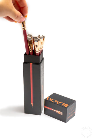 Hand holding a pencil above a black tray with red-tipped and teal pencils