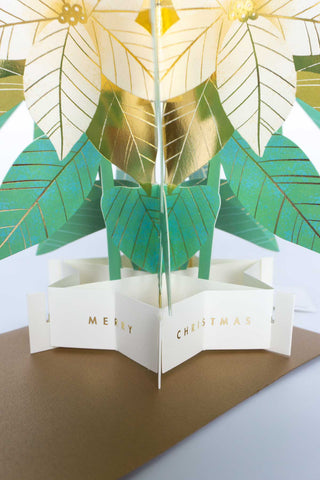 Pop-up Christmas card opened, with green and gold poinsettia leaves and “MERRY CHRISTMAS”