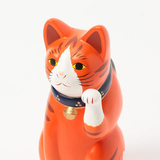 Orange ceramic fortune cat face with yellow eyes, white muzzle, and raised paw