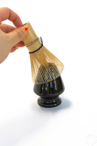 Ceramic matcha whisk stand holding a bamboo chasen whisk with loop handle