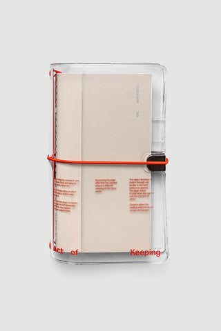Clear vinyl travel notebook cover with beige insert, red elastic band, and black closure clip