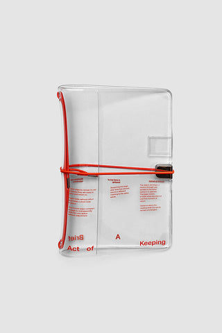 Clear vinyl travel notebook cover with red elastic band, black clips, and pocket insert