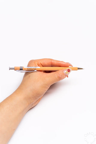 Orange wood ball pen held in hand with metal ballpoint tip facing forward