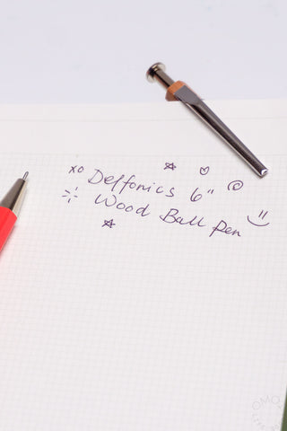 Wood ball pen with gray barrel and metal ballpoint tip, capped with a brown wood end