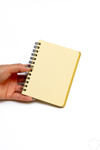 Pocket memo spiral notebook held in hand, cream grid cover with metal rings