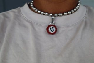Person wearing a chain necklace with a red #15 mini pool ball charm