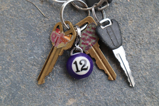 Set of keys with a purple #12 charm on a textured surface