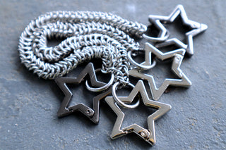 Silver star-maille chain with five dark star charms on gray surface