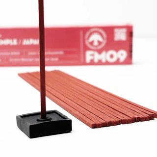 Incense stick upright in black base, red sticks laid beside FM09 box