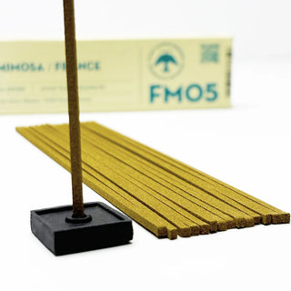 Provence Mimosa incense sticks with lit tip on a small black square holder