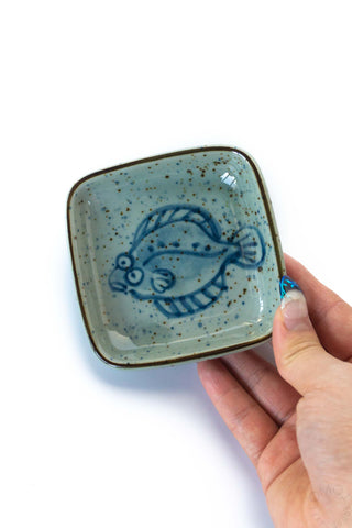 Square ceramic dish, teal speckled glaze with blue flounder motif; held in hand