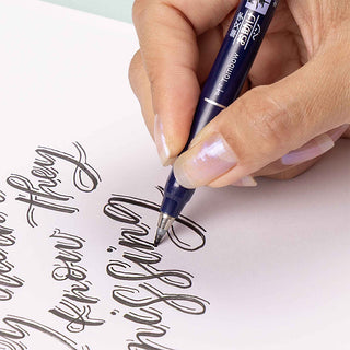 Hand holding a dark blue brush pen creating thin calligraphy strokes