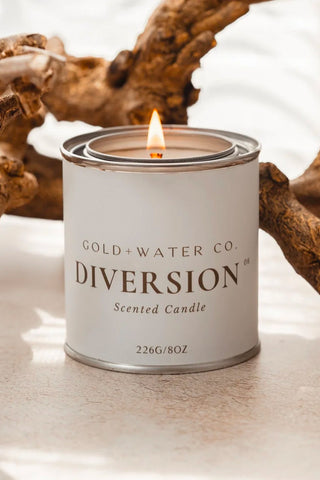 GOLD+WATER CO. DIVERSION scented candle in white metal tin, flame centered on top