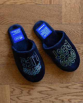 Navy fabric rest room shoes on wood floor, neon-outlined “Good Rest Happier Life” text