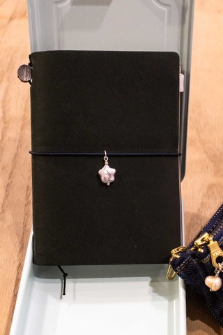 Small pink star pearl charm on a dangling metal chain on a black tag