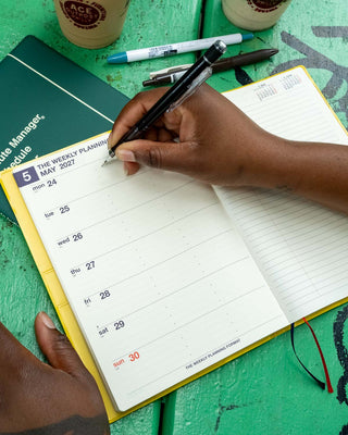 A5 weekly planner open to weekly planning layout with pen writing on the date columns