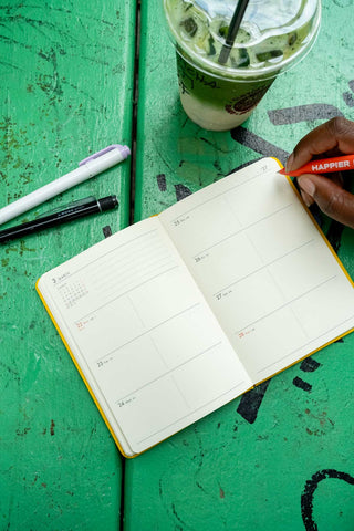 Yellow A6 weekly block planner open to weekly blocks, with pen writing