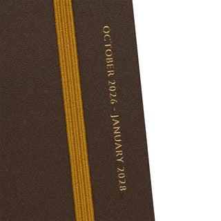 Close-up of slim planner spine with gold embossed year text and yellow fabric binding