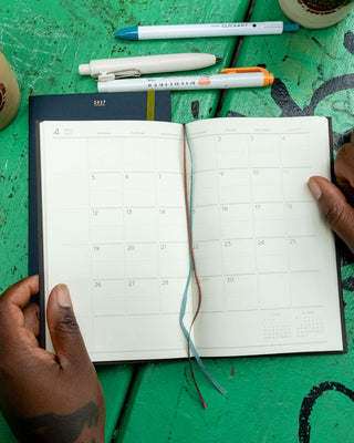 Open monthly planner with two-page 2027 calendar grid, ribbon ties visible