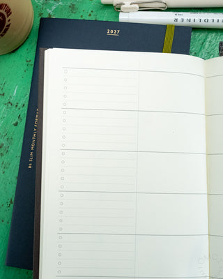 Open navy B6 slim monthly planner with blank weekly grid pages for 2027