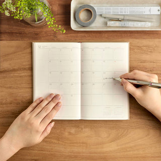 Slim monthly planner open to calendar pages with handwritten notes and pen on desk