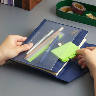 Hands holding blue A5 planner with sticky notes, pen, and pens tucked in