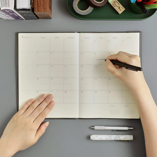 Open A5 monthly calendar planner on desk with handwritten notes and pen