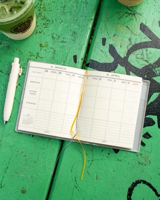 Open weekly planner with yellow ribbon ties and March–April 2027 date grid
