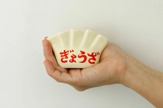 Porcelain dumpling pen holder in cream white, red Japanese characters, held in hand
