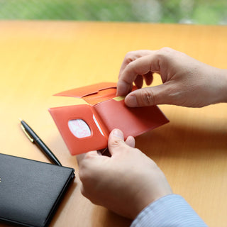 Orange leather card case being fitted by hands on a desk