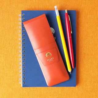 Orange leather-look pen case holding colored pens, with stitched flap and logo patch.