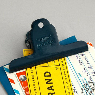Navy steel binder clip securing papers on a desk