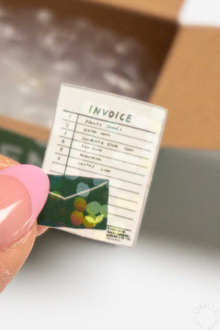 Invoice-style sticker seal label with green and multicolor icons, held by a hand