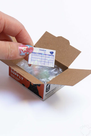 Sticker seal box open with clear wrap and a hand applying a small sticker