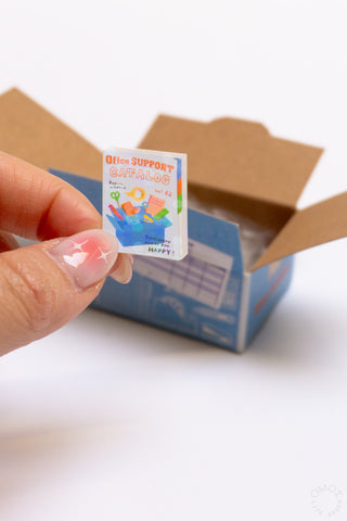 Hand peeling a small label from a blue seafood seal sticker box