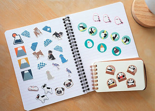 Dog character sticker flakes on an open notebook, with extra stickers in a case