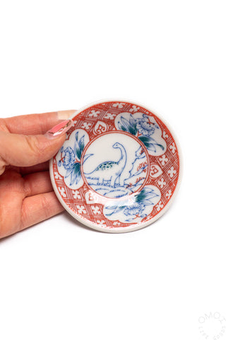 Porcelain mini plate held in hand, red and blue dinosaur print on the face