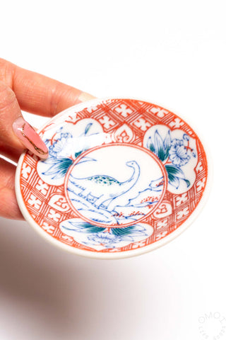 Porcelain mini plate close-up, red and blue dinosaur design on decorated rim